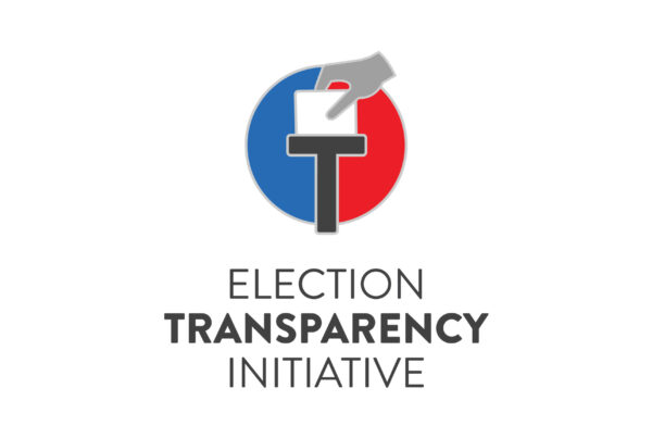 Logo for the Election Transparency Initiative featuring a stylized ballot box with a hand inserting a paper, over a circular red and blue background, and the text Election Transparency Initiative below.