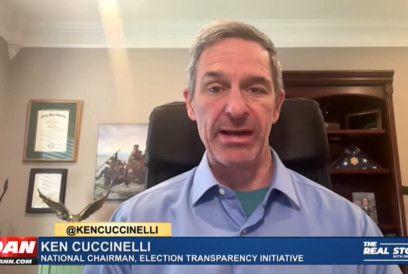A man in a blue shirt speaks during a video interview. Text on screen reads @KENCUCCINELLI Ken Cuccinelli, National Chairman, Election Transparency Initiative, discussing the CA Voter ID Initiative Qualifies for Ballot as SAVE Act debate intensifies on Capitol Hill.